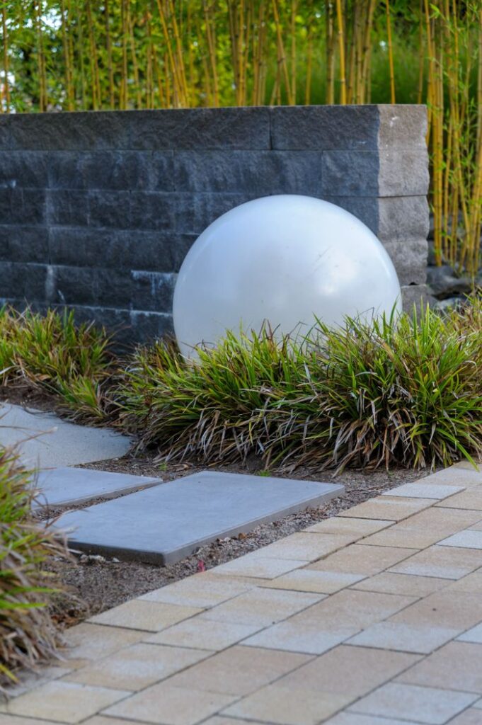 Elegant garden path with decorative stone sphere and bamboo backdrop.